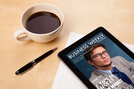 Workplace with tablet pc showing magazine cover and a cup of coffee on a wooden work table close-up